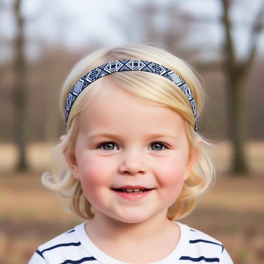 A young girl with blonde hair wearing a blue and white patterned headband is smiling at the camera.