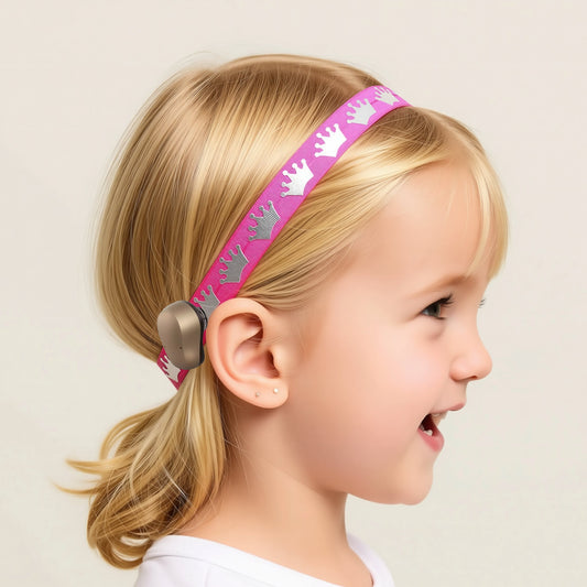 A young girl with blonde hair wearing a pink headband with crown designs.