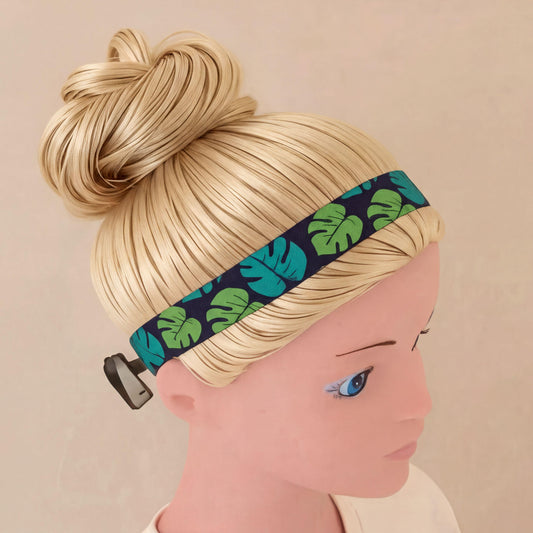 A blonde mannequin head wearing a patterned cochlear implant headband with a black base and green tropical leaf print, shown against a plain beige background.