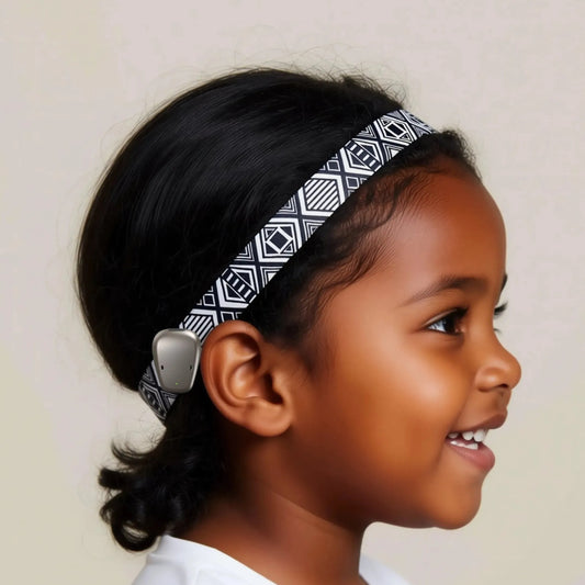 A young girl with a black and white patterned headband is smiling and looking to the side.