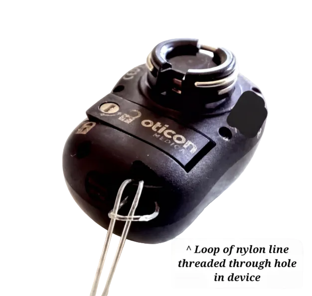 A close-up of a black Oticon Hearing device with a loop of nylon thread threaded through a hole.