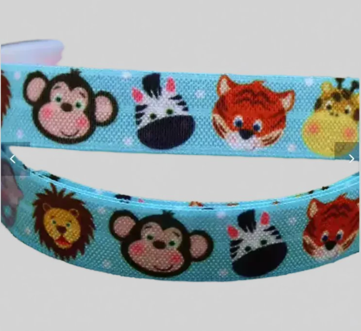 A light blue woven elastic for cochlear implant hearing aid headband featuring a repeating pattern of cartoon animal faces, including a monkey, zebra, tiger, lion, and cat, shown against a plain light gray background.