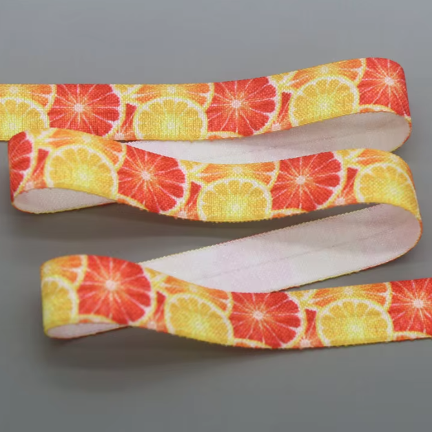 A close-up of a fabric hearing aid headband with a repeating citrus slice pattern in red, orange, and yellow, shown against a solid gray background.