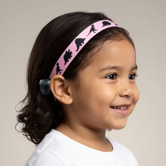 A young child wearing a pink wide cochlear implant hearing aid headband with black dinosaur silhouettes, shown in profile against a plain light beige studio background.