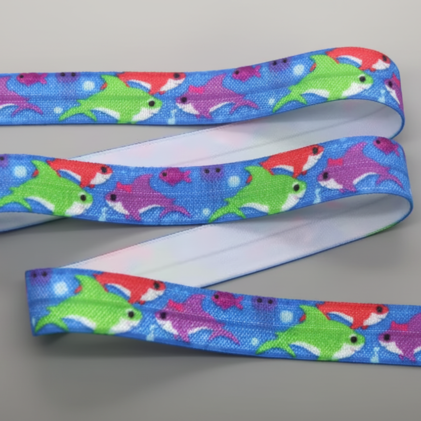 A close-up of a blue elastic for hearing aid headband, featuring a colourful pattern of cartoon sharks in green, red, and purple.