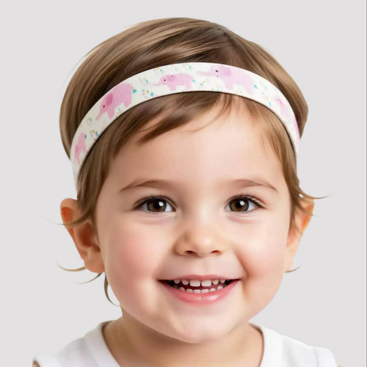 A smiling young child wearing a white hearing aid headband with a pink elephant pattern, photographed against a light gray studio background.