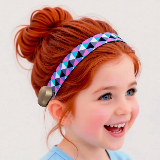 A smiling young girl with red hair in a high bun wears a geometric patterned headband with a ponto baha hearing device, set against a plain light background.