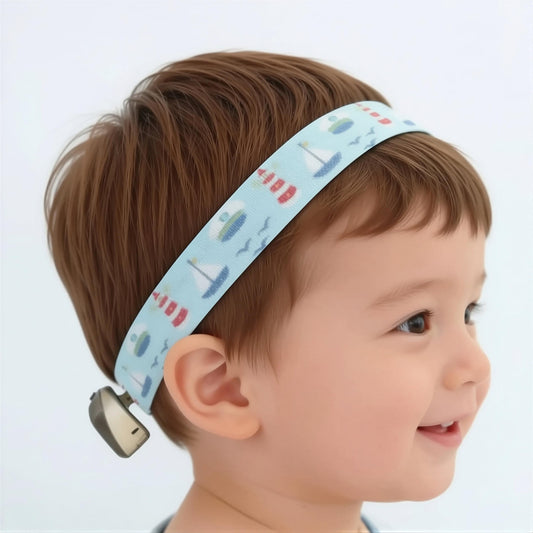 A close-up side profile of a young child wearing a light blue fabric ponto baha softband headband with a nautical print of sailboats, seagulls, and red-and-white striped buoys.