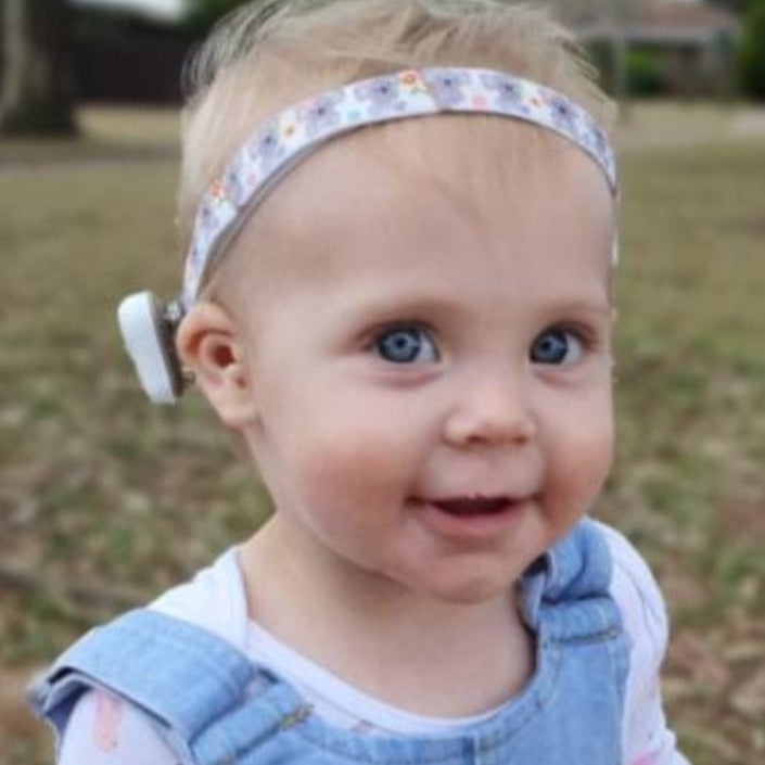 Baby wearing a ponto baha hearing aid softband headband and denim overalls outdoors