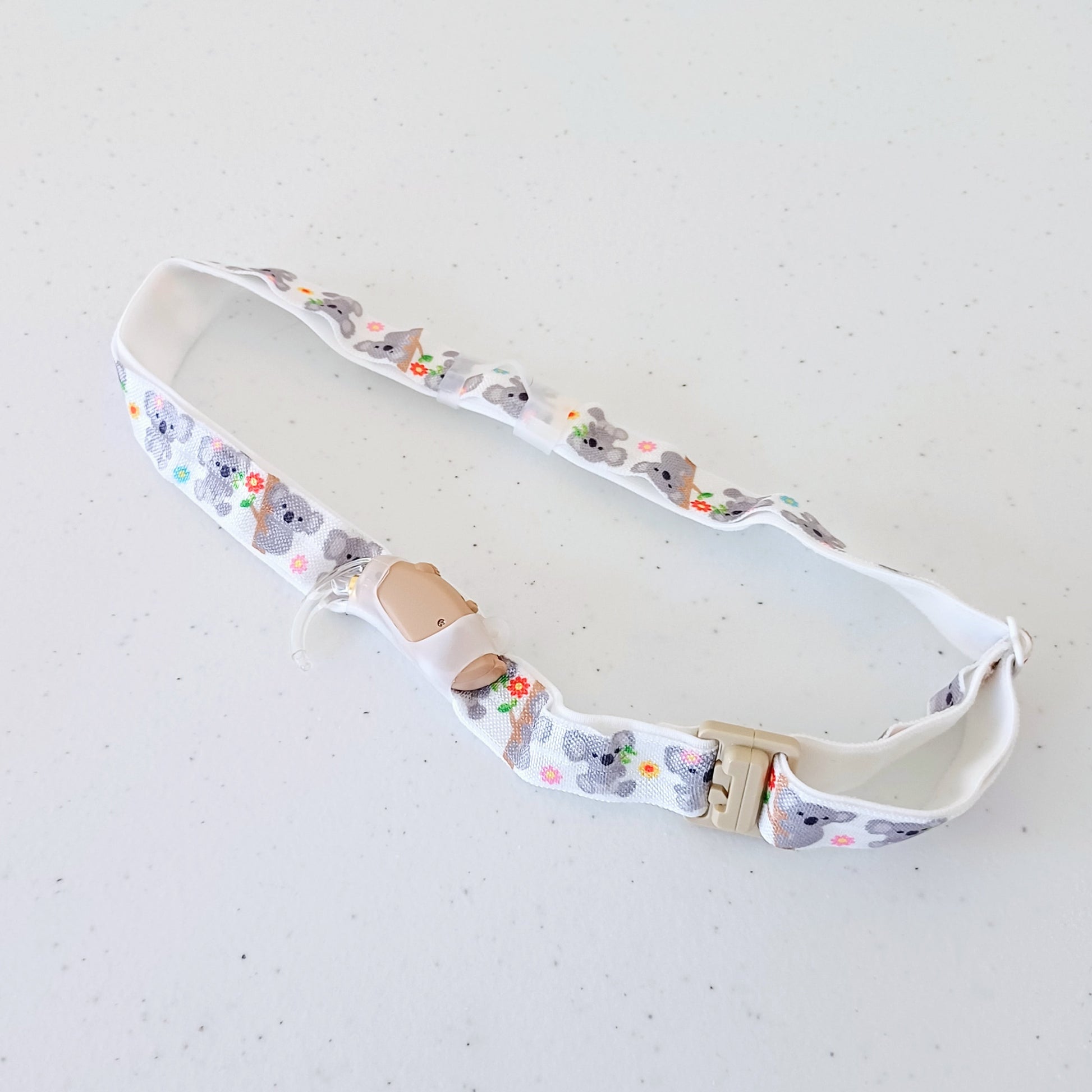 Hearing aid headband with cartoon koala design on a light gray background