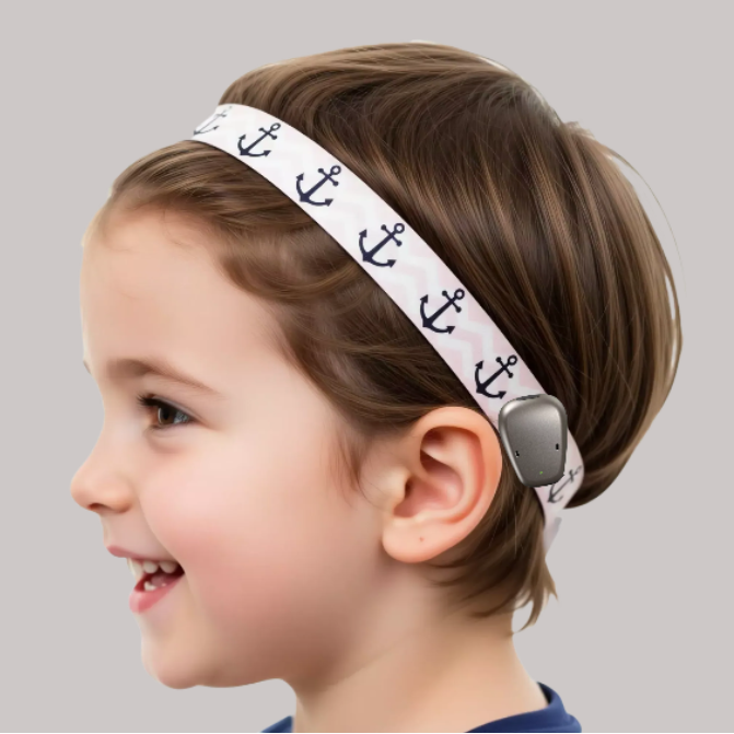 A young child wearing a grey hearing aid cochlear implant headband decorated with a repeating navy blue anchor pattern.