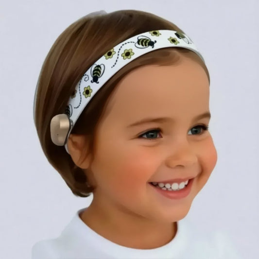A young child wearing a ponto baha hearing aid headband decorated with a black and yellow bee pattern, shown in a close-up portrait against a light gray background.