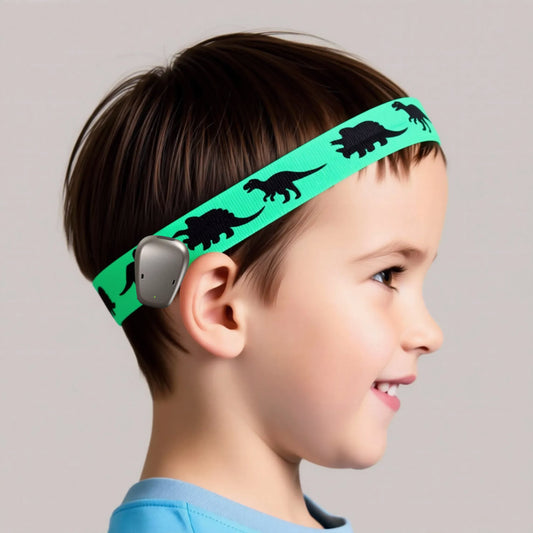 A child in profile wearing a green hearing aid headband with black dinosaur silhouettes.