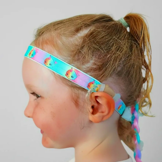 Child wearing a colourful hearing aid headband with ponytails on a plain background