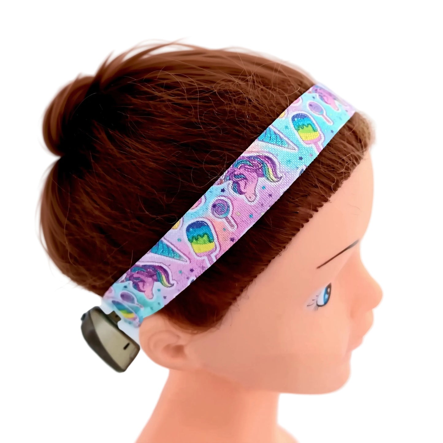 A close-up of a kids' fabric ponto baha softband with a colorful unicorn and popsicle pattern, shown on a mannequin head with brown hair.
