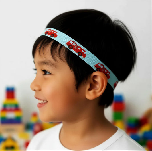A young child in profile wearing a light blue hearing headband with a repeating pattern of red fire trucks, set against a softly blurred background of colorful toys.