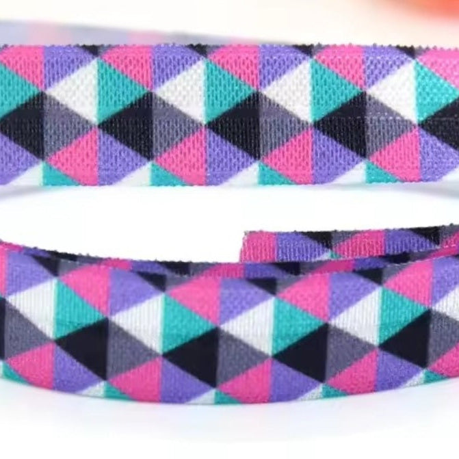 A close-up of elastic for a hearing aid headband featuring a colourful geometric triangle pattern in pink, purple, teal, black, and white on a white background.