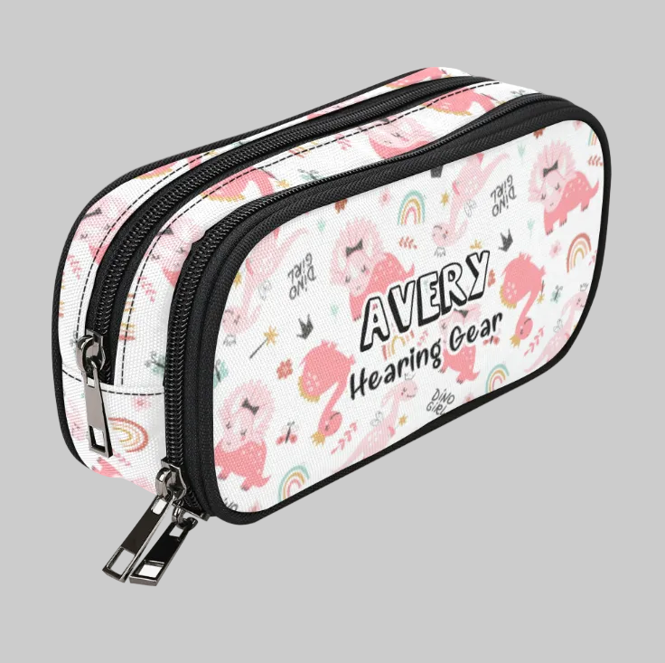 A white double-compartment cochlear implant hearing aid storage case with a pink cartoon llama and unicorn pattern, featuring the text 'AVERY Hearing Gear' on the front, set against a solid gray background.