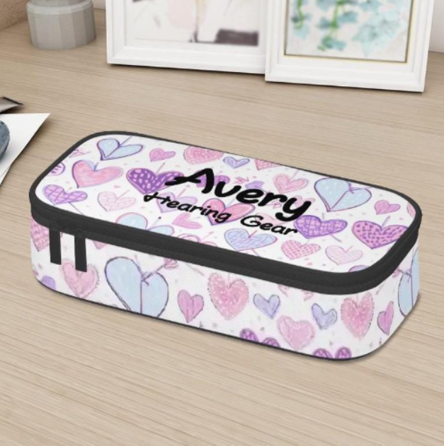 A rectangular zippered storage case for cochlear implants or hearing aids, with a white background, decorated with a pattern of pink, purple, and blue hearts. The top features the personalized text 'Avery' and 'tearing gear' in black script