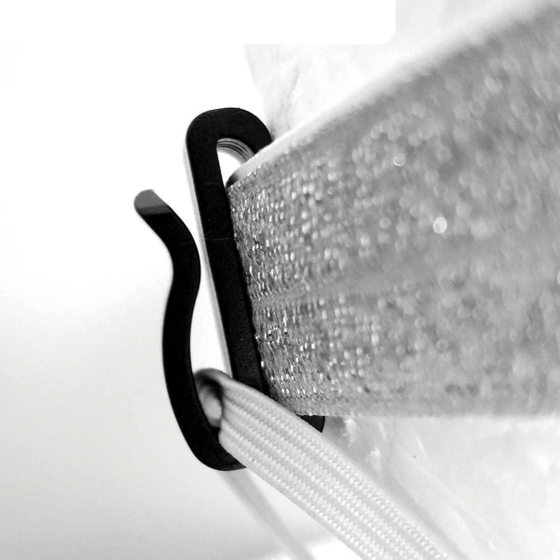 Close-up of a black S-shaped hook or clip attached to a glittery silver strap, with a white braided cord visible against a plain light background.