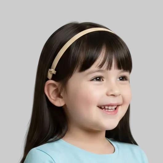 A young girl with long dark hair is shown in profile wearing a beige cochlear implant  headband
